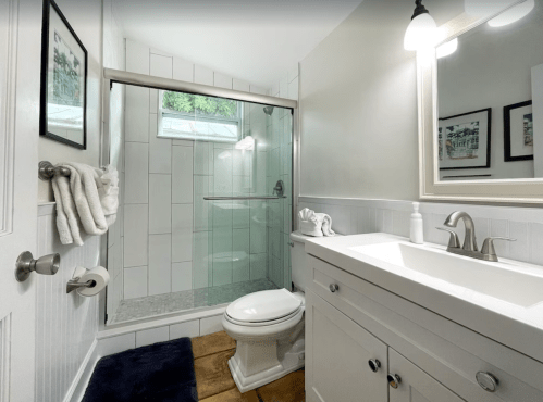 A modern bathroom featuring a glass shower, white vanity, and neutral decor with framed artwork on the walls.