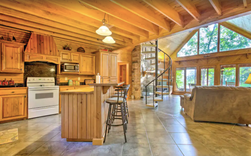 Cozy wooden cabin interior with a spiral staircase, modern kitchen, and large windows overlooking nature.