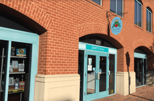 A brick building with a turquoise door and sign reading "Hooray" above, featuring a display window with books.
