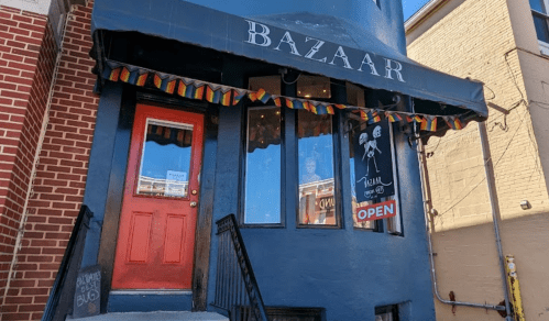 A blue building with a red door and an "Open" sign, featuring colorful bunting above the entrance.