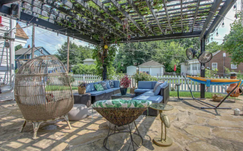 Cozy outdoor patio with a pergola, comfortable seating, hanging plants, and a hammock in a green backyard setting.