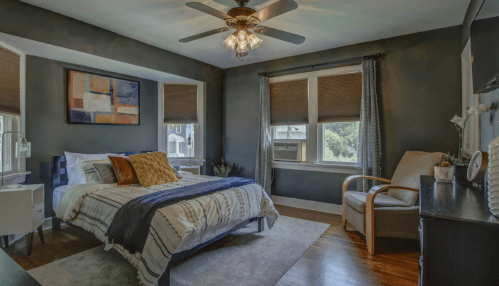 Cozy bedroom with a bed, armchair, and large windows, featuring dark walls and modern decor.