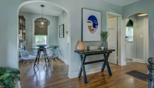 A cozy entryway with a dining nook, featuring a round table, clear chairs, and modern decor in a light gray setting.
