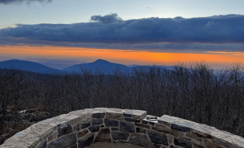 A scenic view from a stone overlook, showcasing mountains and a colorful sunset with clouds in the sky.