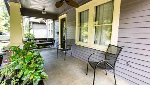 A cozy porch with two black chairs, potted plants, and a ceiling fan, featuring a welcoming entrance.