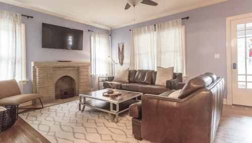 Cozy living room with a brown leather sofa, a coffee table, and a TV mounted on a light purple wall.