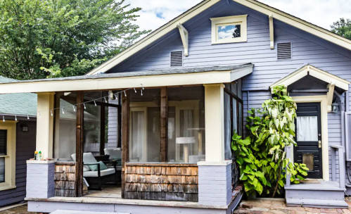 A charming purple house with a front porch, surrounded by greenery and a cozy seating area.
