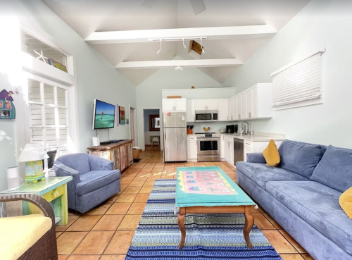 Bright, airy living space with a blue sofa, colorful coffee table, and modern kitchen appliances. Natural light floods the room.