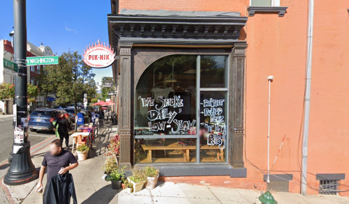 A restaurant exterior with a large window displaying a sign that reads "We Smoke Daily, Low & Slow" in chalk.