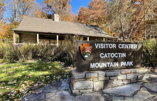 A stone building with a sign reading "Visitor Center, Catoctin Mountain Park" surrounded by autumn foliage.