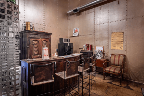 A cozy, vintage-style office with wooden furniture, a small kitchenette, and metal walls.