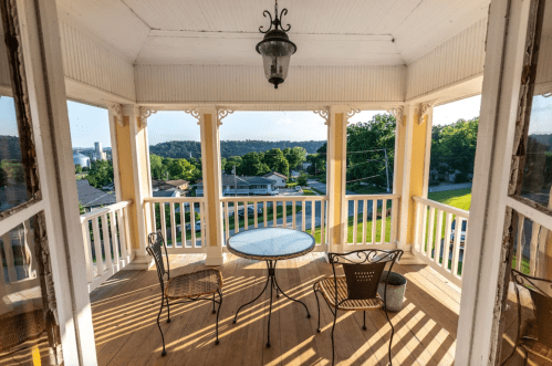 A cozy porch with a round table and two chairs, overlooking a green landscape and distant buildings.