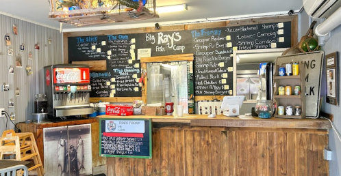 Interior of Big Ray's Fish Camp with a menu board, drink station, and rustic wooden decor.