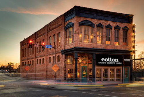 A brick building at sunset with large windows, featuring a sign for "cotton creative southern cuisine."