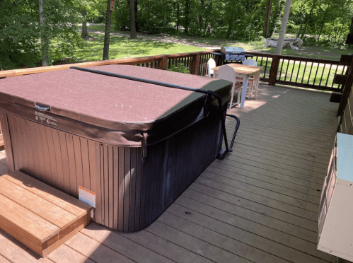 A hot tub on a wooden deck surrounded by trees, with outdoor furniture in the background.