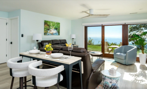 Modern living room with a dining area, leather seating, and large windows showcasing a scenic view. Bright and inviting decor.