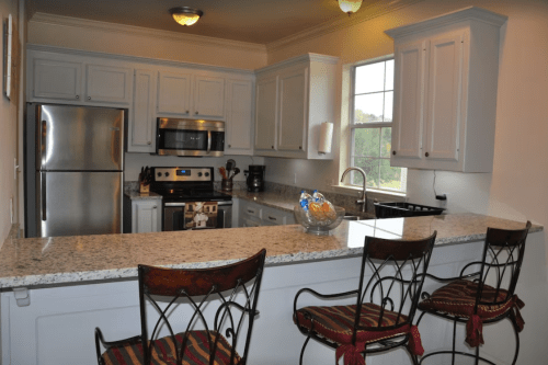 Modern kitchen with stainless steel appliances, granite countertops, and bar seating with decorative chairs.