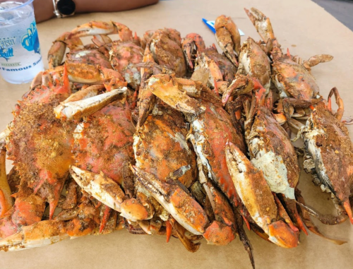 A pile of seasoned crabs on a brown paper surface, with a drink in the background.