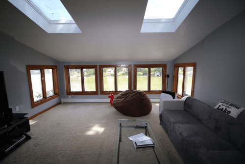 Cozy room with large windows overlooking a lake, featuring a bean bag, sofa, and coffee table. Bright and airy atmosphere.