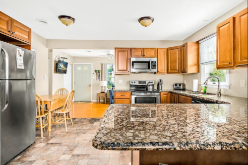 A modern kitchen with wooden cabinets, granite countertops, stainless steel appliances, and a dining area.