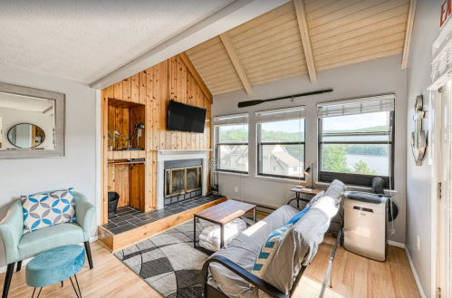Cozy living room with a fireplace, large windows, and lake view, featuring a sofa, coffee table, and armchair.