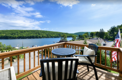 A scenic view from a deck overlooking a lake, surrounded by green hills and blue skies.