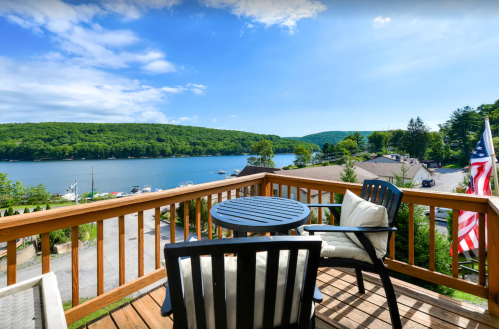 A scenic view from a deck overlooking a lake, surrounded by green hills and a clear blue sky.