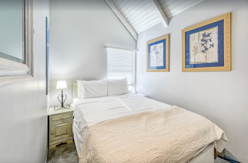 Cozy bedroom with a double bed, bedside lamp, and framed artwork on white walls under a sloped ceiling.