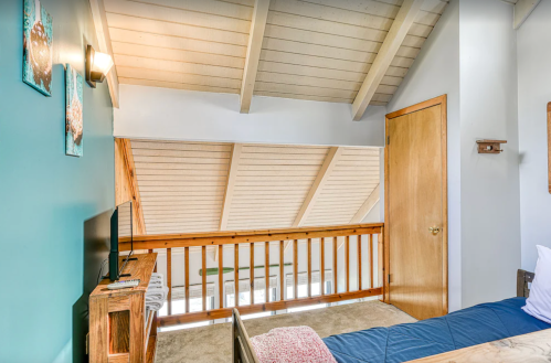 Cozy room with a wooden railing, sloped ceiling, and a TV, featuring blue walls and decorative wall art.