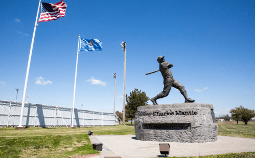 Statue of baseball player Mickey Mantle with flags in the background, honoring his legacy as a great teammate.