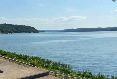 A serene view of a calm river surrounded by green hills under a clear blue sky.