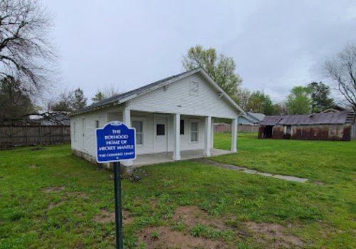 A small white house with a sign reading "The Richmond Home of Vincent Waffle" in a grassy area with trees.