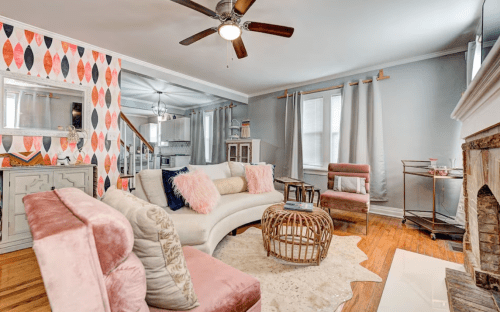 Cozy living room with a patterned accent wall, plush seating, and a decorative fireplace. Bright and inviting atmosphere.