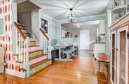 A cozy interior featuring a staircase, dining area, and modern decor with warm wood floors and colorful wall accents.