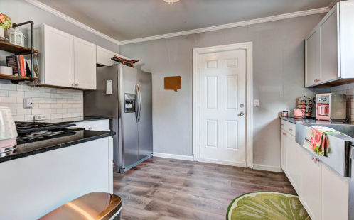 A modern kitchen with gray walls, white cabinets, stainless steel appliances, and a decorative rug on the floor.