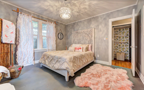 Cozy bedroom with a patterned bedspread, soft rug, and decorative curtains, featuring a chandelier and floral wallpaper.