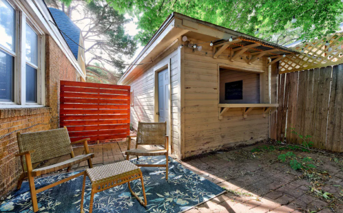 Cozy outdoor space with two chairs, a rug, and a wooden shed surrounded by greenery and a wooden fence.
