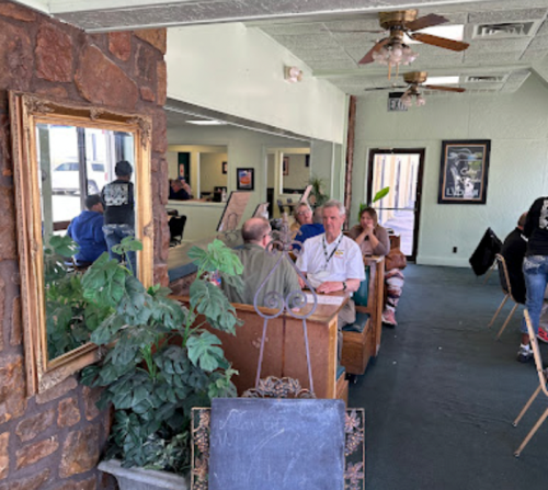 A cozy restaurant interior with patrons seated at tables, plants, and a large mirror reflecting the space.