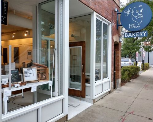 Exterior of Lost Larson Bakery, featuring a sign, large windows, and a display of baked goods at the entrance.