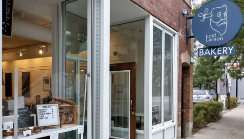 Exterior of Lost Larson Bakery, featuring a sign, open door, and display of baked goods in the window.