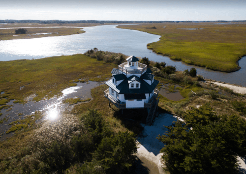 Aerial view of a unique, multi-level house on stilts surrounded by marshland and a winding river.