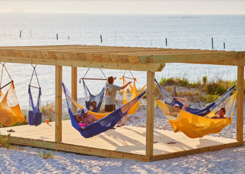 A beachside wooden structure with colorful hammocks, where people relax and enjoy the ocean view.