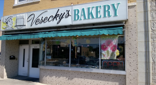A storefront of Vesecky's Bakery with a bright sign, open hours displayed, and colorful decorations in the window.