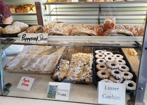 A display case filled with various baked goods, including poppyseed slices, apple slices, blueberry slices, and Linzer cookies.