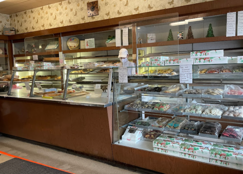 A bakery display filled with various pastries and treats, with a staff member in a mask behind the counter.