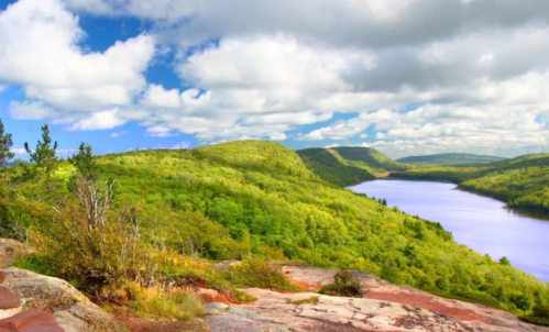 A scenic view of lush green hills and a calm lake under a bright blue sky with fluffy clouds.