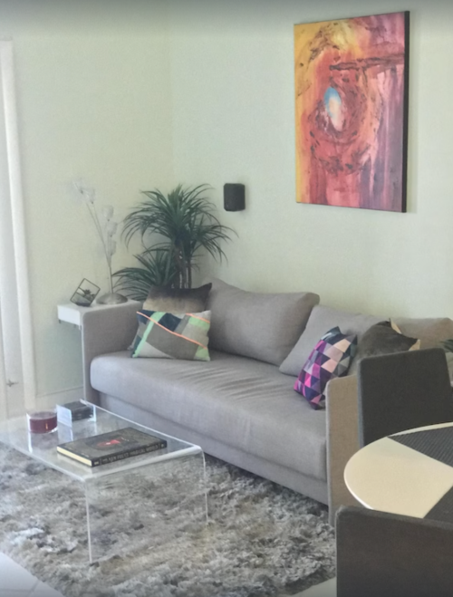 A modern living room featuring a gray sofa, colorful pillows, a glass coffee table, and an abstract painting on the wall.