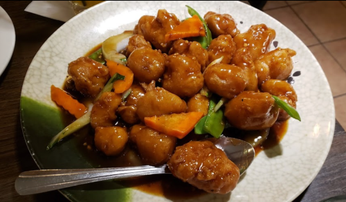 A plate of sweet and sour chicken with vegetables, garnished and served with a spoon.