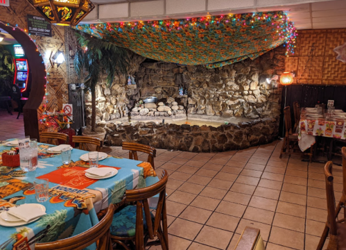 A cozy restaurant interior featuring a stone wall, colorful tablecloths, and festive lights overhead.