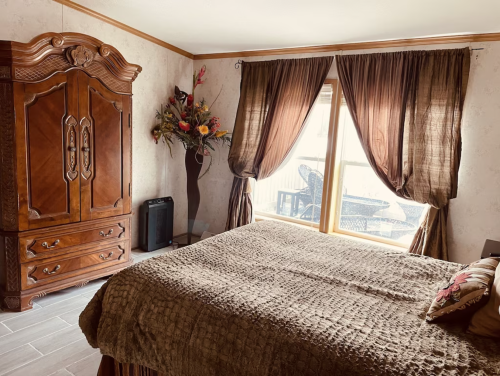 Cozy bedroom with a large wooden wardrobe, a textured bedspread, and curtains framing a window with outdoor seating.